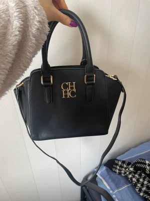 Väska  - Svart handväska med gulddetaljer från Carolina Herrera. Osäker på om den är äkta. Perfekta skick. 