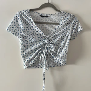 Vit topp med blå blommor - Vit topp med blå små blommor, med band i mitten som man justerar själv.