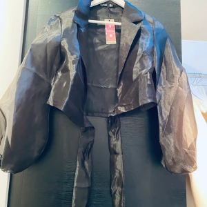 Blus svart croppad. - Svart croppad blus "organza". Ballongärmar. Knyt i midjan fram eller bak på ryggen. Genomskinlig. Aldrig använd. 