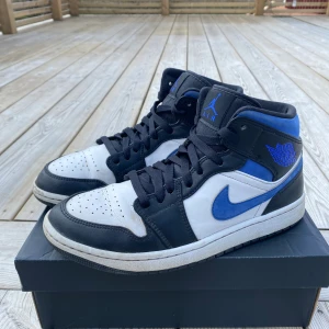 Nike Air Jordan 1 Mid  - Nike Air Jordan 1 Mid i använt men ok skick. Liten bit av sulan vid ena hälen är borta. I övrigt hela. Köpta på Restocks så 100% äkta. Har kvitto att visa upp vid köp. Skosnören ej original. Orginallåda medföljer, dock lite trasig i kanterna.   Färg: Blue/white/black Storlek: 42,5 Nypris: 2700:- 