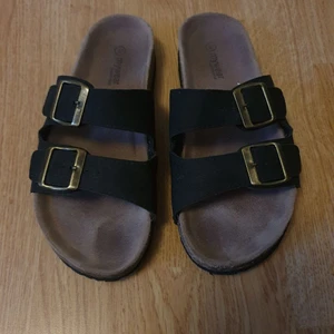 Tofflor - Lädertofflor av träfiber och självsjusterande remmar. Har haft ytterst få gånger (2-3 gånger inomhus). Passar utmärkt som present samt att de är riktigt sköna och är mjuka att gå eftersom de har en väldigt mjuk sula. Köpte de för 250kr