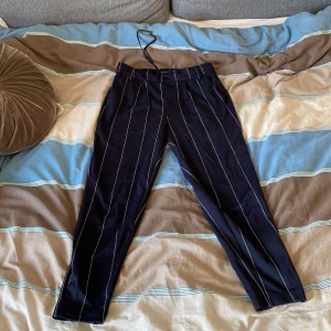 Kostymbyxor i strl 30/XS från ONLY - Jättefina marinblå kostymbyxor från ONLY. Väldigt fin passform och oerhört mjuka och sköna. Finns justerbara snören i midjan och kan således justeras. Relativt stretchig midja. Bra skick men finns tecken på användning (små trådar kring resårbandet i midjan) 