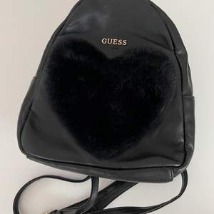 black mini backpack from Guess with a faux fur heart patch at the front. fully lined. adjustable shoulder straps. 
