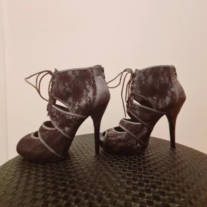 Sexiga stiletter med grå spets - Mörkgrå sexiga stiletter med öppen tå fram, hög mörklila stilettklack och grå snören. Även dragkedja bak på hälen för enklare påtagning. Knappt använda då de var lite för stora för mig.