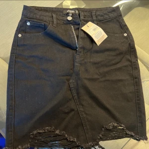 Svart jeanskjol med slitningar från Missguided HELT NY OANVÄND - Svart jeanskjol med slitningar från Missguided i storlek 34 men passar även 36. HELT NY OANVÄND MED PRISLAPPEN KVAR.