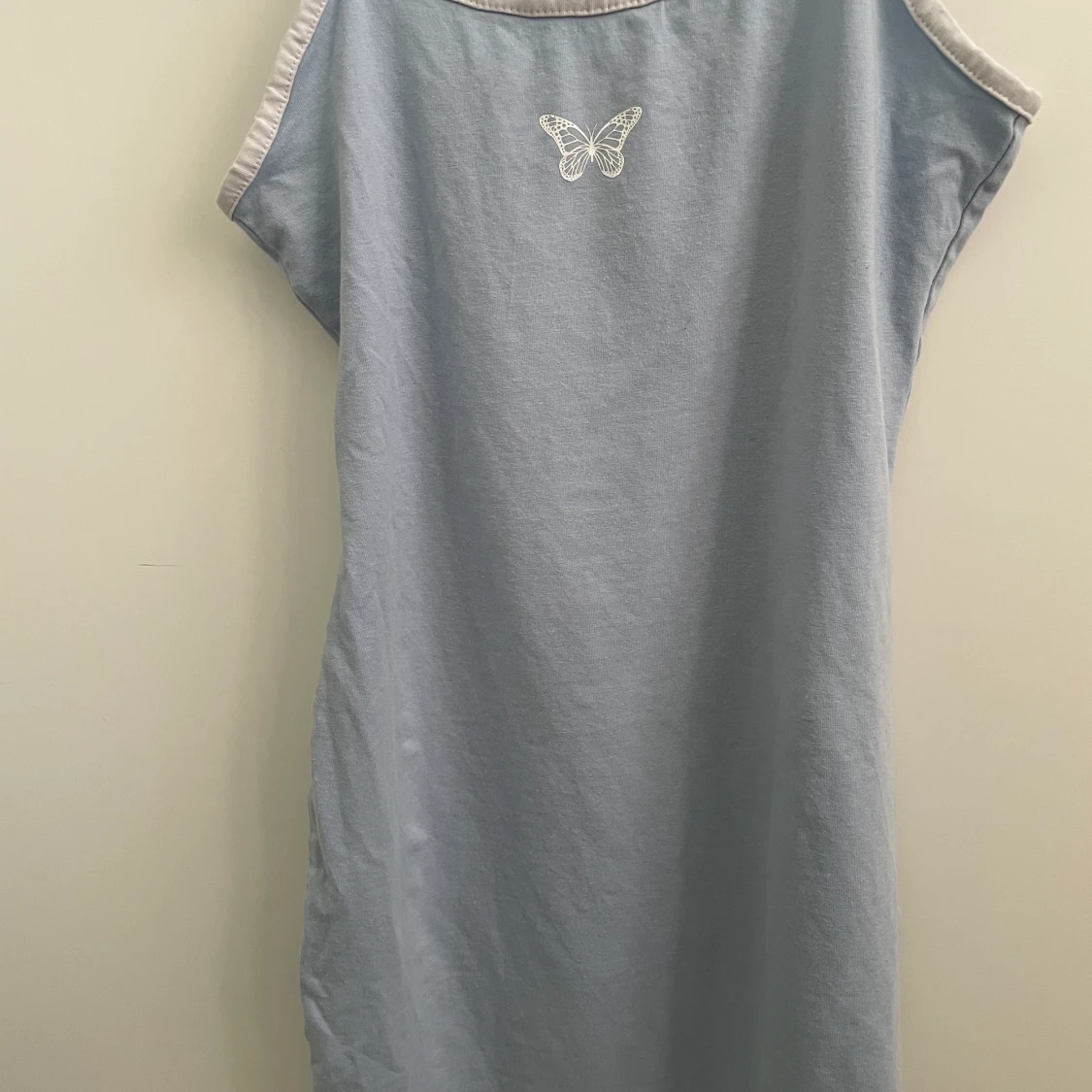 Ljusblå klänning får H&M med en vit tryckt fjäril på bröstet 