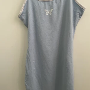 Ljusblå klänning får H&M med en vit tryckt fjäril på bröstet  - Figursydd och kort i modelle