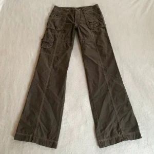 Cargobyxor - Lågmidjade utsvängda gröna cargobyxor, från märket Mexx! Massa coola fickdetaljer! Jag är 173 cm, midjemåttet är 74 cm och innerbenslängden 81 cm ❤️‍🔥(uppsydda, går att göra längre)