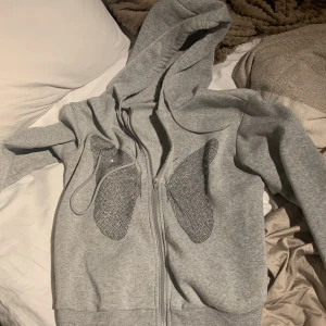 GRÅ FJÄRILS ZIP UP HOODIE - Hej! Säljer denna super snygga zipupen i grå! Skit snyggt fjärils tryck av små stenar i glittrigt svart😫Totalt nyskick men säljer för den tyvärr aldrig används! Frakt på 25kr🫶🏼 Ordinariepris: 189kr Mitt pris: 89 kr