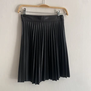 Plisserad kjol i fake-skinn - Superfin plisserad minikjol i fakeläder från märket Bershka. Kjolen är 47cm lång och har 64cm i midjevidd.  Använd en gång och i bra skick! 