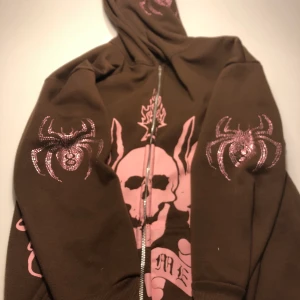 Brun Y2k rhinestone hoodie - En cool rhinestone hoodie som inte kommer till användning. Köpt från något TikTok märke, rhinestone format som spindlar på båda sidorna av luvan och på båda armbågarna också ett coolt rosa tryck mitt på tröjan