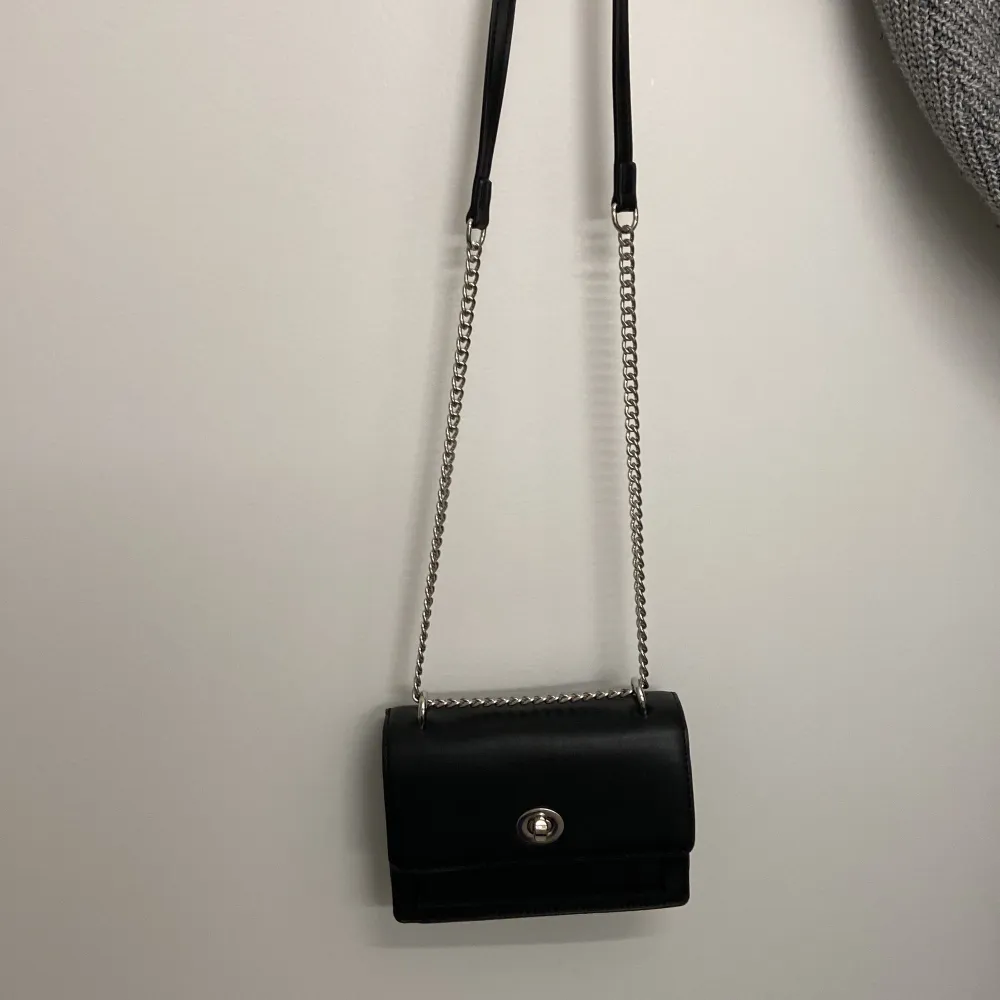 En svart handväska med silvrig kedja, helt oanvänd och i nyskick, den har två stora fack med ett mindre fack i ena, super söt fast säljer pga kommer inte till användning . Väskor.