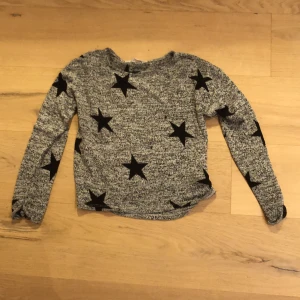 Grå långärmad tröja med svarta stjärnor - Grå långärmad tröja kan vara bra att ha någonting under! Inkluderar ej frakt eller Swish. Tar Swish 