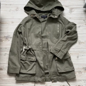 Khakigrön militärjacka med luva <3 - Oanvänd khakigrön militärjacka med luva och snörning i midjan 🖤 Jackan kan stängas med dragkedja och knappar. Jackan har två fickor med knappar och en ficka med dragkedja. Storlek 34 men passar även 36. 