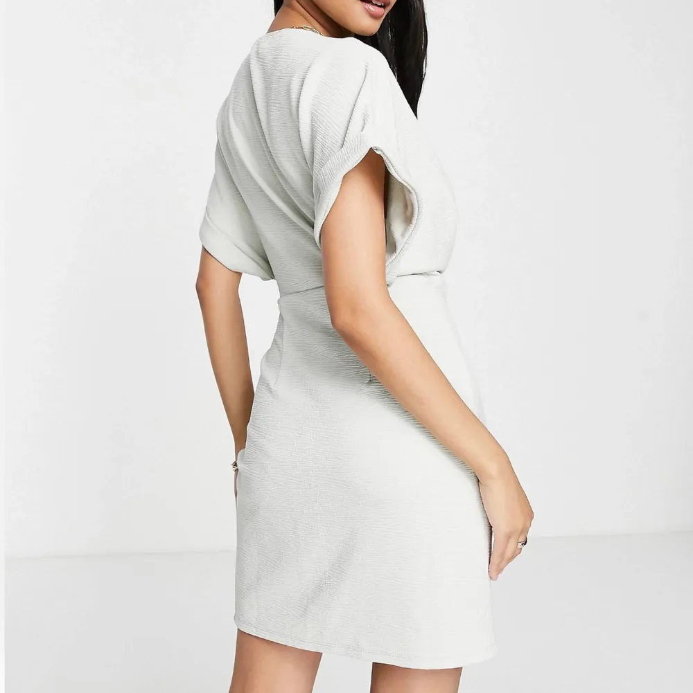 Ljusgrå texturerad mini-omlottklänning med korta ärmar. Skön och snygg klänning i nytt skick, oanvänd! Stretchigt material. Säljer den då den inte kommer komma till användning och returtiden har passerats. Klänningar.