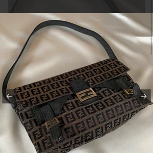 Fendi baguett bag - Funderar på att sälja min älskade fendi väska i deras ikoniska bruna zucchino mönstrade kanvas och svarta skinndetaljer.  Köpte den på vintage by ebba och är såklart 100% äkta.                       Färg: Brun och svart med guldfärgade metalldetaljer. Material: Jacquardvävd kanvas och skinn. Mått: 24 x 14 x 6 cm, axelband: 49 cm  Skick överlag: Gott skick Smått solblekt, repor och guldfärgen är avskavd till viss de. Skriv gärna för fler bilder