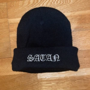 Mössa Satan  - En snygg, rejäl och cool svart mössa från Darkside Clothing med texten Satan broderat på. Perfekt att bära året runt och vid alla tillfällen. Varm och skön.