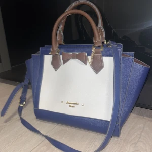 Samantha Vega väska - Samantha Vega väska, knappt använd och ser helt ny ut. Många olika fack, fickor och en korthållare. Vit, blå med bruna och guldiga ditaljer.