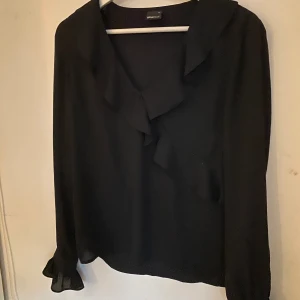 Svart blus - (Dåliga bilder pågrund av ljuset mot en svart tröja) En svart blus med volanger (se bilderna) Nypris 300 Mitt pris 100
