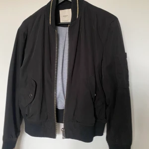 Bomberjacka från Mango - Säljer en svart bomberjacka från Mango, i storlek small. Jackan är i bra skick, dock lite nopprig i ärmarna, se sista bilden. ﻿Mjukt material inuti.  ﻿Stängs med dragkedja.  ﻿Gulddetaljer.  ﻿Två framfickor.