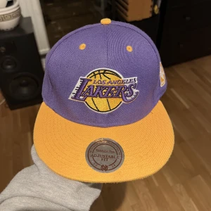 Lakers Keps  - Lakers Keps, Nba, Mitchell &Ness, Hardwood Classics Finns inga skador på den, klistermärket kvar, Ljuset på bilderna får kepsen att se blekt ut eller som att färgen gått bort men den är färglad och har fortfarande samma färg.