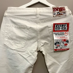 Evisu Jeans - SKRIV FÖR FLER BILDER ❤️Vita Jeans med vita detaljer och prislapp kvar från Evisu (European Edition). Nyskick. Lågmidjade och utsvängda. obs: ungefärliga mått: Midjemått: 83cm. Innerbenslängd: 84cm. Grenhöjd: 19cm. 