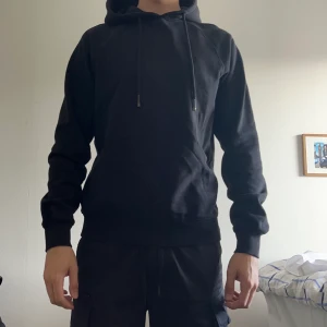 Hel svart hoodie med litet svart tryck på framsidan.  - Helt ok skick, inte använd jätte mycket men den har använts ett tag. Köpt på carlings för 600 kr. Passar både S och M