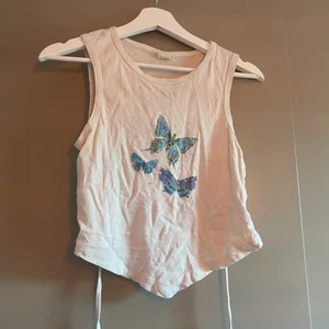 Topp med fjärilsmotiv! - Jättesöt topp med öppen rygg från Urban Outfitters! Den är i toppenbra skick då den knappt har kommit till användning. Storlek M, men kan bli större och mindre tack vare de justerbara banden i ryggen <333