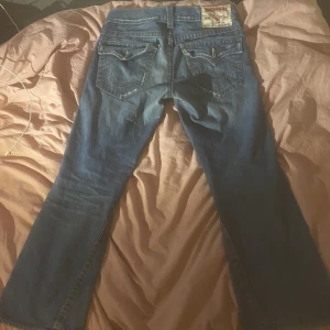 True Religion Jeans - Säljer ett par snygga vintage true religion jeans med lite bootcut som tyvärr är för små för mig. Köpte dem begagnat, bra skick lite slitage vid knä och lår.  Innerben 78cm Ytterben 101cm Midja (rakt över) 45cm Pris är inte fast :)
