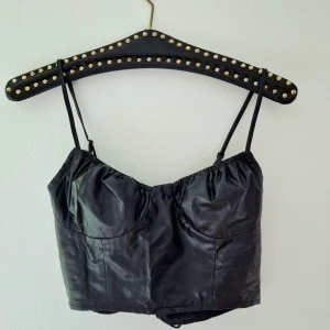 Fake läder/latex - Sjukt snygg fake-läder crop top i stretchigt tyg. Ruffles runt bysten, där mina pannkakor tyvärr inte fyller ut. Därav får denna vandra vidare. Snygg snörning bak i ryggen dessutom 🐈‍⬛🦇