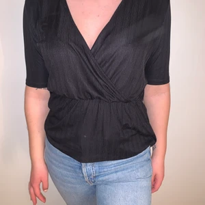 Svart blus - Svart blus med v-ringning som går omlott, resor i midjan. Stretchigt material. 