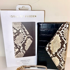 Clutch Iphone Ideal Of Sweden: Helt ny - Helt ny Clutch från Ideal Of Sweden, aldrig använd och inte öppnad (förutom för att ta bild till annonsen).   Köptes för 500 kr. Fick dubbla exemplar i julklapp. Är jättenöjd med clutchen jag valt att behålla och använder varje dag.  Väldigt användbar, fungerar som väska, korthållare, skydd för mobilen och mobilfodral i ett och samma föremål!  Kompatibel med iPhone 11 och iPhone XR  * Stängs med magnetisk knapp på framsidan * 3 kortfack plus 1 större öppning för kontanter * Inkluderar ett svart 