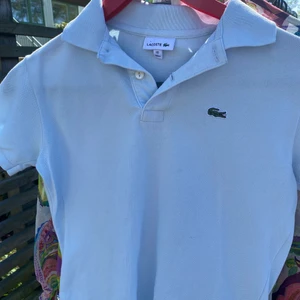 Ljusblåa Lacoste piké  - Det här är en ljusblå piké från Lacoste som egentligen är för ett barn i 10 årsåldern då det är storlek 140 för barn men den funkar även om man har storlek xs-s och går ner till höfterna.