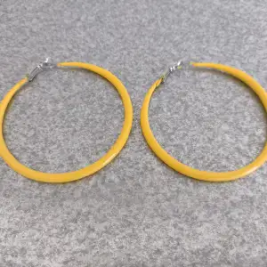 Gula hoops i metall. Ca 7 cm i diameter. Ett litet märke/färgbortfall på det ena örhänget.