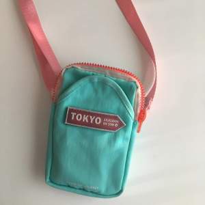 Mintgrön liten väska från kawaii.se. Den rosa remmen är justerbar. Har ett huvudfack och en framficka. Dimensioner: bredd 11cm längd 16cm djup 4cm. Priset inkluderar frakt, meddela vid frågor!