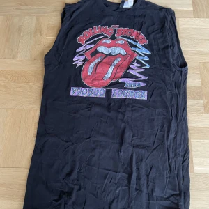 Rolling Stones klänning - En svart Rolling Stones klänning från H&M. Den är bredaxlad, armhålen är 28cm i diameter och från armhåla till slutet är den 54cm. Använd en gång, nytt skick. Trycket är lite speciellt; det blir mer slitet för varje tvätt.