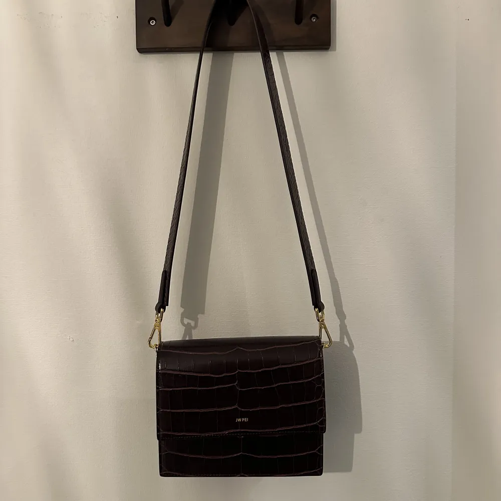 Säljer min fina crossbody-väska från Jw Pei i veganskt skinn/konstläder. Aldrig använd och med lappar kvar. Avtagbar axelrem. Nypris ca 750 kr.  Väskan mäter 20cm x 15.5cm x 8cm och bandet är ca 43 cm. Väskor.