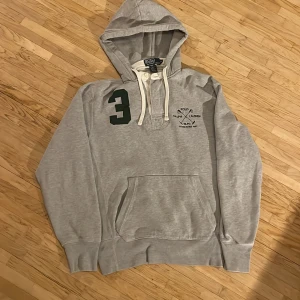 Grå Polo Hoodie - En grå Polo Ralph Lauren hoodie, inga fläckar förekommer men knapparna är lite slitna