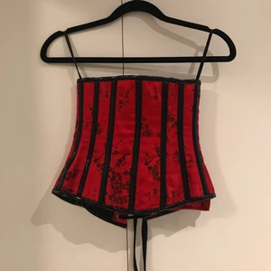 Röd/svart korsett  - Köpt secondhand! Snygg röd/svart korsett med små blommor som detaljer.Jag brukar ha S men denna var för liten på mig, passar säkert bättre på någon med XS. Finns lite skada på sista bilden där framme och där bak. Det är bara att fråga om fler bilder! 😌