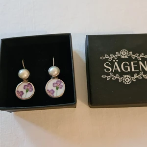 Sägen örhängen silver 925 oanvända - Örhängen i silver 925 från Sägen. Porslin och pärla. Aldrig använda. Text på örhängena: "Sägen 925". Mått: 2,5 cm + delen i örat.