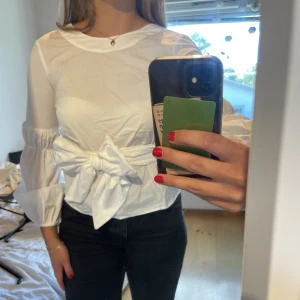 Vit Blus/Skjorta  - Söt knytblus i vitt med detaljer på armarna. Blusen har långa band som man kan knyta framtill som jag gjort eller hur man vill. Från Carin Wester, köpt för 599kr och endast använd en gång vid speciellt tillfälle. Säljer för 60kr, hör av dig vid frågor💕