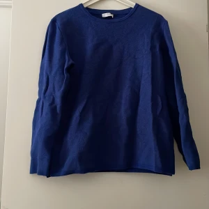 Stickad tröja - En blå/svart stickad tröja med öppning på midjan. Skick 9/10 inga skador.
