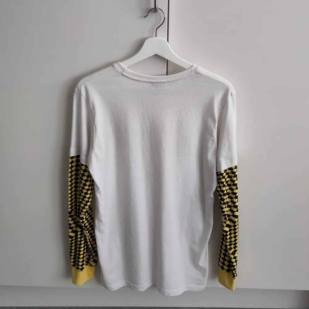 Vit långärmad t-shirt med gul- och svartrutiga ärmar. Unisex storlek medium. Märket är Airwalk men köpte den på Depop för några år sen. Det är en ljus fläck på vardera ärm men syns knappt när tröjan är på 🙂 . T-paidat.