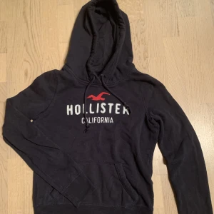 Hollister hoodie - Fin hollister hoodie i marinblå, den är i storlek S men skulle säga den lutar mer åt XS. Säljes pågrund av ej används!