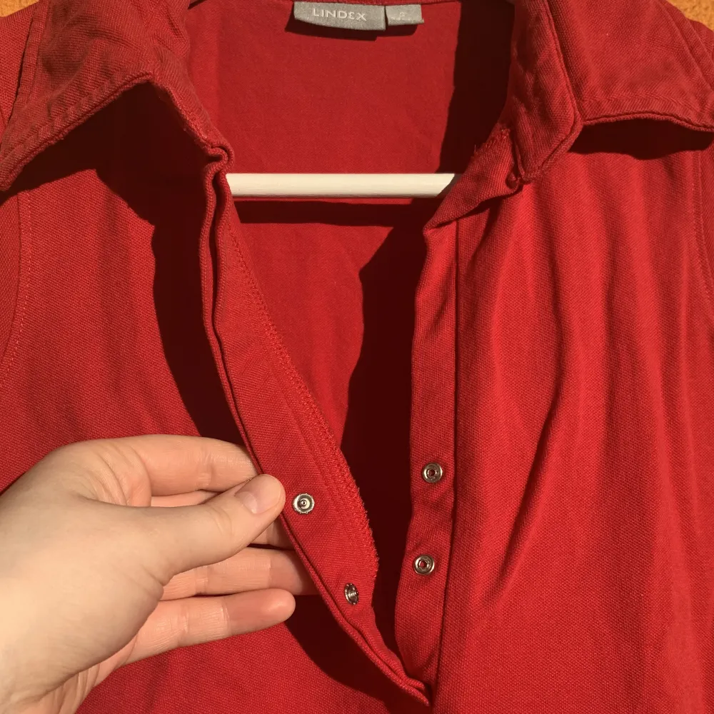 Rött linne med krage och v-urringning med knappar. I bomullsmaterial med lite stretch. Tajt passform. Om du har frågor eller vill se fler bilder är det bara att skicka iväg ett meddelande:). Toppar.
