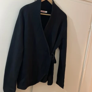 Stickad svart kofta - Svart ny kofta med omlottknyt i sidan. 