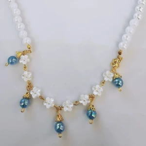 Vitt skimrigt halsband  - Vit skimrig akrylpärla, guldiga detaljer (ej äkta guld, kan innehålla nickel), blå skimrig akrylpärla. 