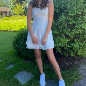 Vit klänning - Säljer en vit klänning med små blommor som kan fungera som studentklänning. Använd endast en gång så är i mycket fint skick och har justerbara axelband som knyts i rosetter 💕