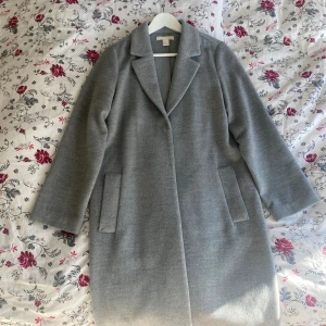 Lång grå kappa H&M - Superfin lång grå kappa från H&M✨ På mig täcker den knäna och går ner till mitten av vaden (jag är 161cm lång). Mysigt tyg, något tunn. Perfekt till våren🌸 Strl 34, passar även 36! Fint skick!