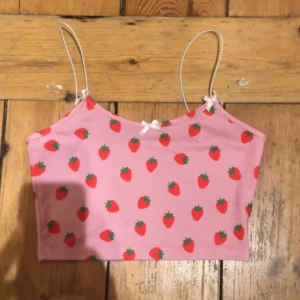 Croppad jordgubbsmöntrad top  - En fin rosa jordgubbsmönstrad crop-top med rosetter i bra skick för att vara från SHEIN. Säljer då den inte kommer till användning längre💘 kontakta vid fler frågor eller intresse vid att köpa!!🍓🍓